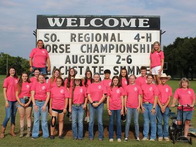 Group in pink shirts in front of sign: "WELCOME" "SO. REGIONAL 4‑H HORSE CHAMPIONSHIP AUGUST 2-6"