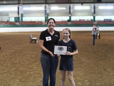 Woman and girl standing in an arena holding a plaque reading "Junior Sportsmanship Award"