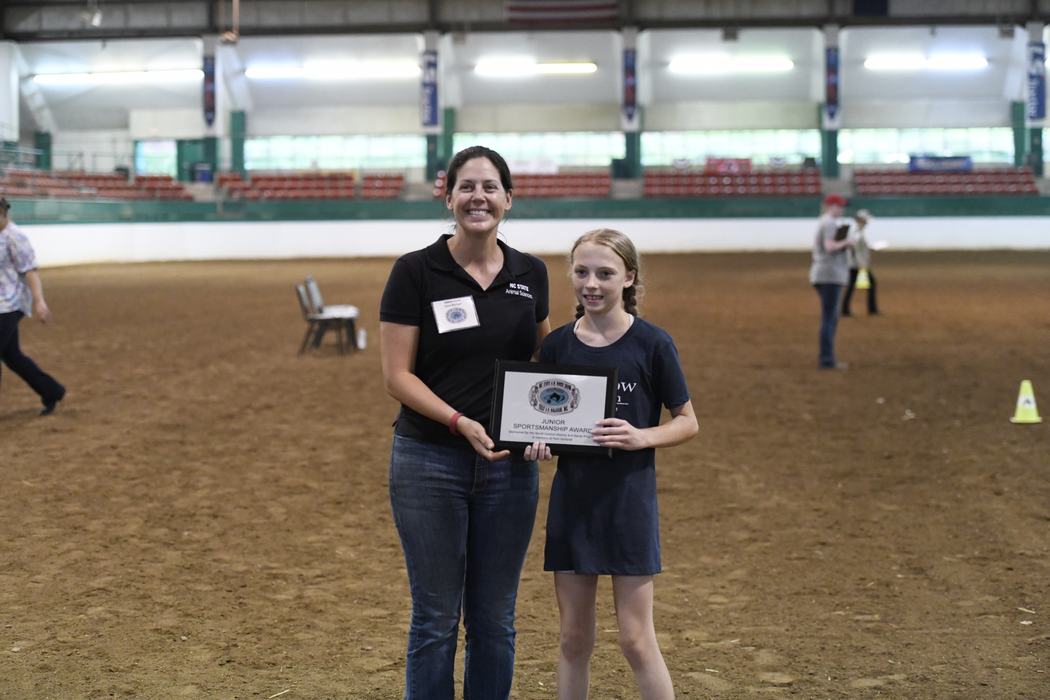 Woman and girl standing in an arena holding a plaque reading "Junior Sportsmanship Award"