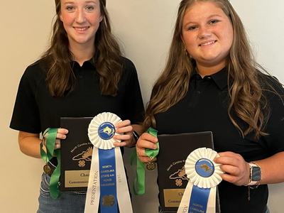 Two young women holding plaques, medals, and blue-and-white ribbons reading "North Carolina State 4‑H Horse Program"