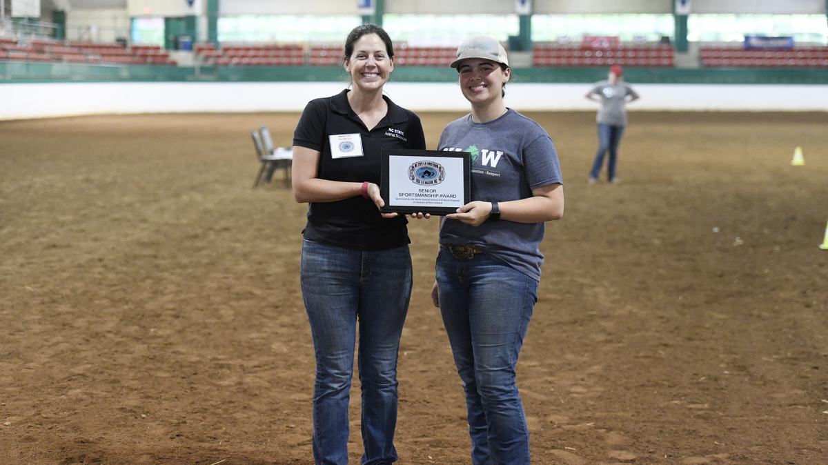 Two people standing in an indoor arena holding a plaque reading "SENIOR SPORTSMANSHIP AWARD."