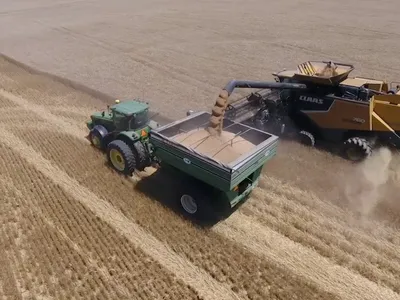 Combine harvester unloading grain into tractor trailer in harvested wheat field