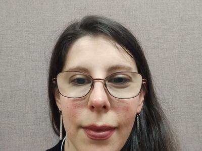 woman with brown hair and wearing glasses with a half smile