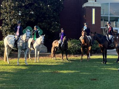 Equestrians on horses holding ribbons outside a brick arena building