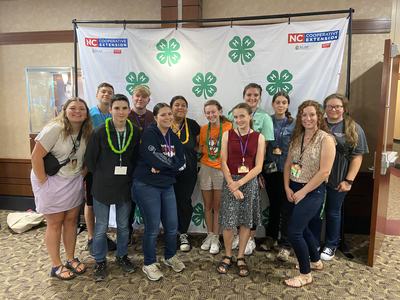 Thirteen young people posing before a 4‑H backdrop with "NC Cooperative Extension" logos