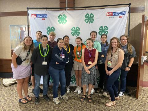 Thirteen young people posing before a 4‑H backdrop with "NC Cooperative Extension" logos