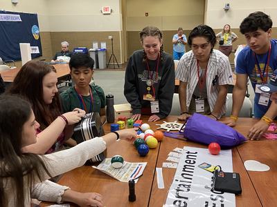 Group of teens gathered around a table with colorful balls and a sign reading "Entertainment"