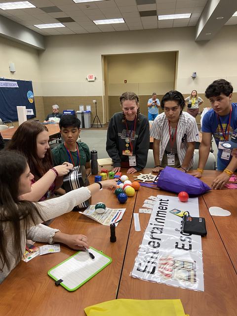 Group of teens gathered around a table with colorful balls and a sign reading "Entertainment"