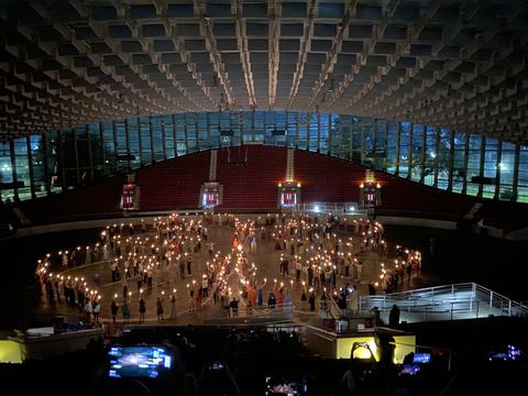 Indoor arena floor with people forming spirals while holding lit torches