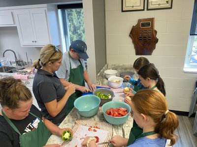 Group of children and an adult at a kitchen counter chopping and preparing vegetables.