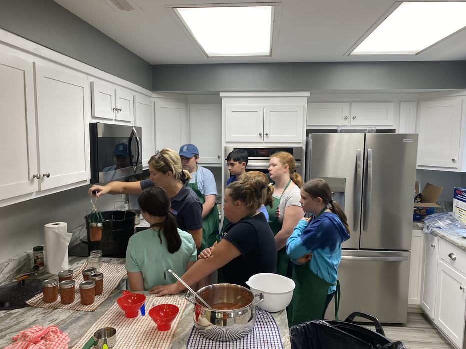 Adult removing a jar from hot water while a group of children watch in a kitchen