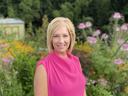 Woman standing in garden wearing bright pink sleeveless top with hands clasped