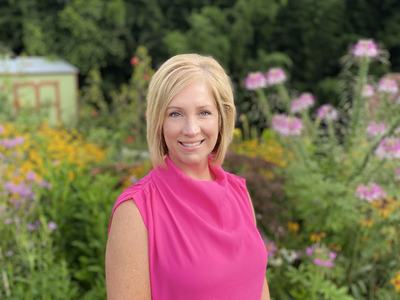 Woman standing in garden wearing bright pink sleeveless top with hands clasped