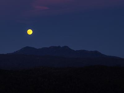 Full moon rising above a dark mountain ridge at dusk