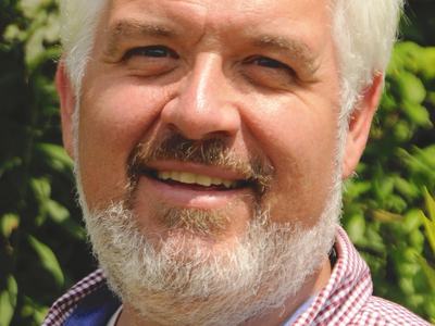 Middle-aged man with white beard wearing red checkered shirt, smiling outdoors
