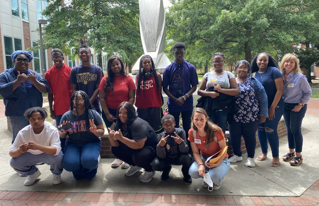 A group of children and adults pose in front of a statue.