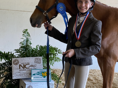 Young rider holding horse with blue ribbon and medal beside "got to be NC Agriculture" boxes