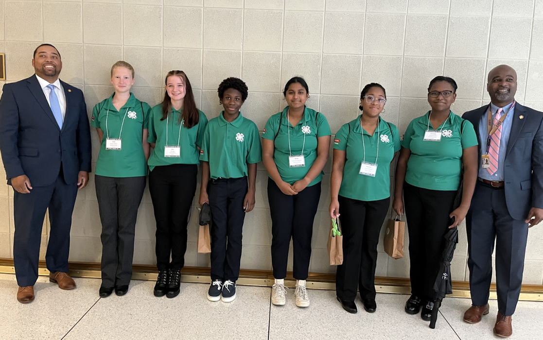 A group of children in green 4-H Shirts pose between two men in suits.