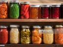 Mason jars of preserved vegetables and jams arranged on wooden pantry shelves