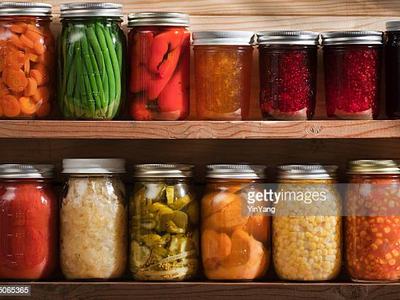 Mason jars of preserved vegetables and jams arranged on wooden pantry shelves