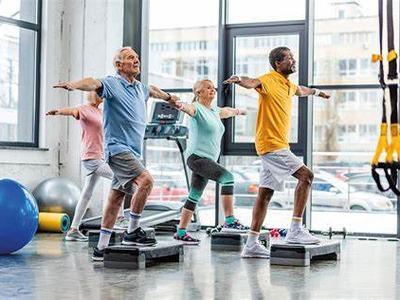 Four adults performing step-platform balance exercises with arms extended in a gym