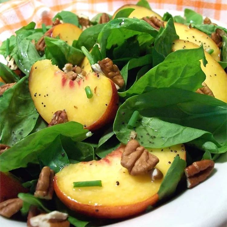 Spinach salad with peach slices, pecans, poppy seeds, and chives