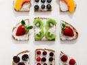 Nine cream-cheese toasts in a grid topped with peach, blueberries, kiwi, strawberries, cherries, raspberries