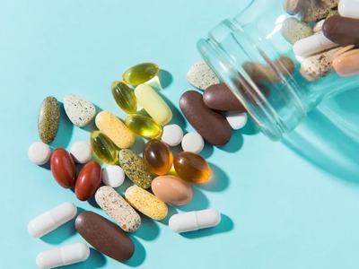 Glass jar tipped, spilling assorted pills and capsules on a turquoise surface