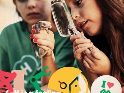 Two girls examining a lizard with a magnifying glass; text "4-H is a feeling." and "I ♥" 4‑H clover