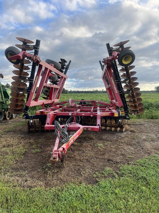 A disk tiller stored at the edge of a field. The arms of the tiller are vertical. 
