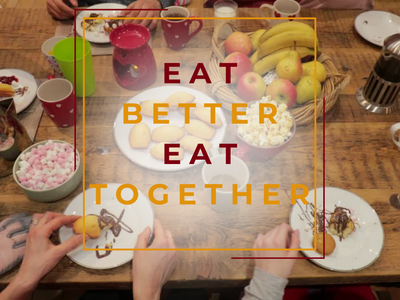 Hands reaching for food at a table with overlay text "EAT BETTER EAT TOGETHER"
