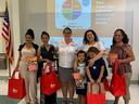 Six adults and two children holding red EFNEP bags and cookbooks before a MiPlato (MyPlate.gov) slide.