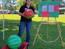Person holding a watermelon-patterned ball beside a wagon of balls and a hoop game board outdoors
