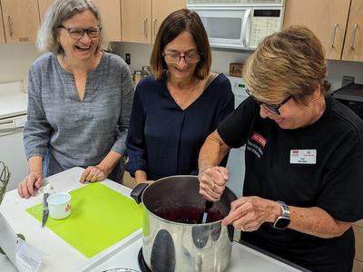 Three women in a kitchen stirring a large pot on a stovetop