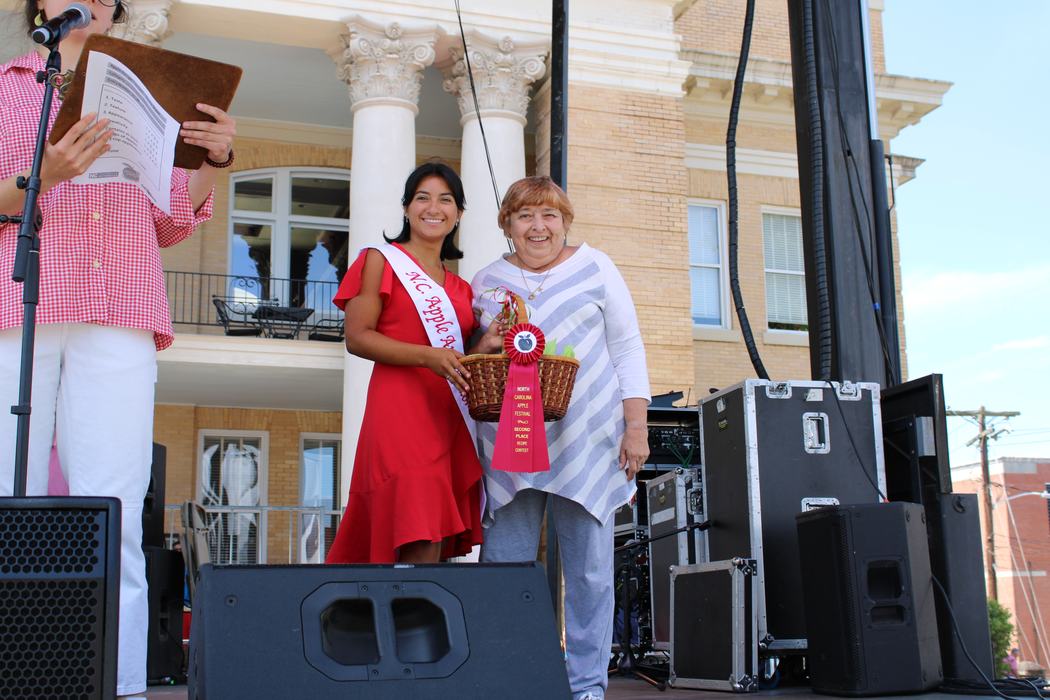 Woman on the left handing gift basket to woman on the right. 