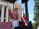 Person holding large trophy and speaking at microphone; woman beside wearing sash "NC Apple Ambassador"