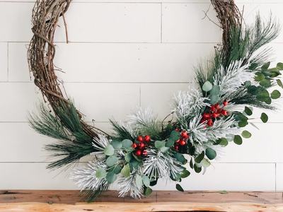 Grapevine wreath with frosted pine, eucalyptus, and red berries above wooden mantel