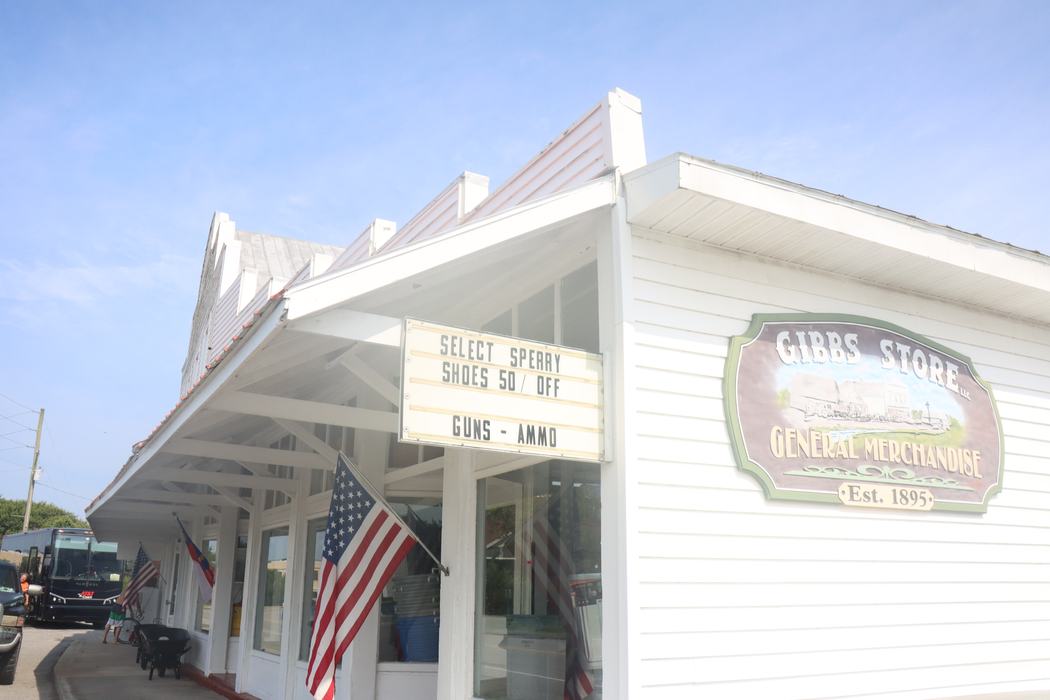 White general store with American flag and sign: "Shoes 50% off; Guns - Ammo"