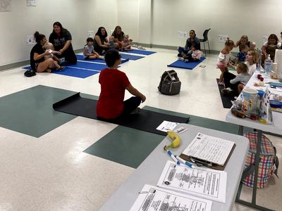 Instructor seated on yoga mat leading parents with infants and toddlers on mats in a classroom