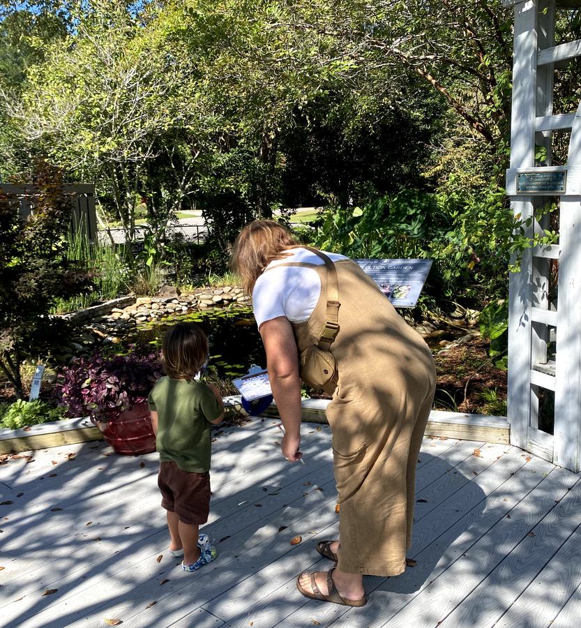 A small child and their guardian looking at garden plaques. 