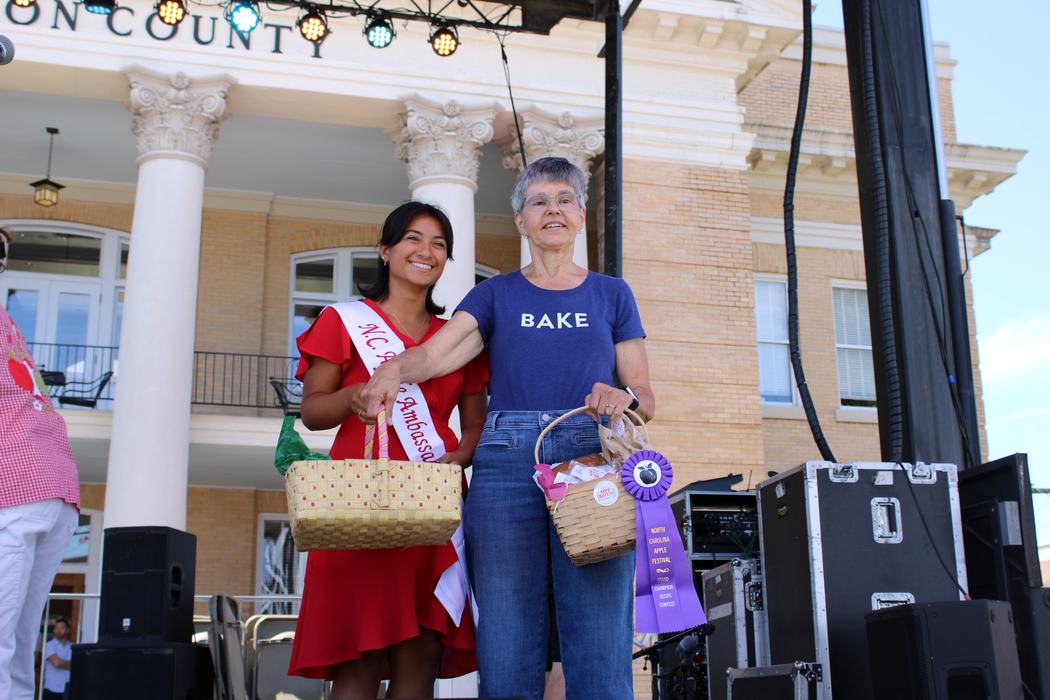 Woman on the left handing gift basket to woman on the right. 