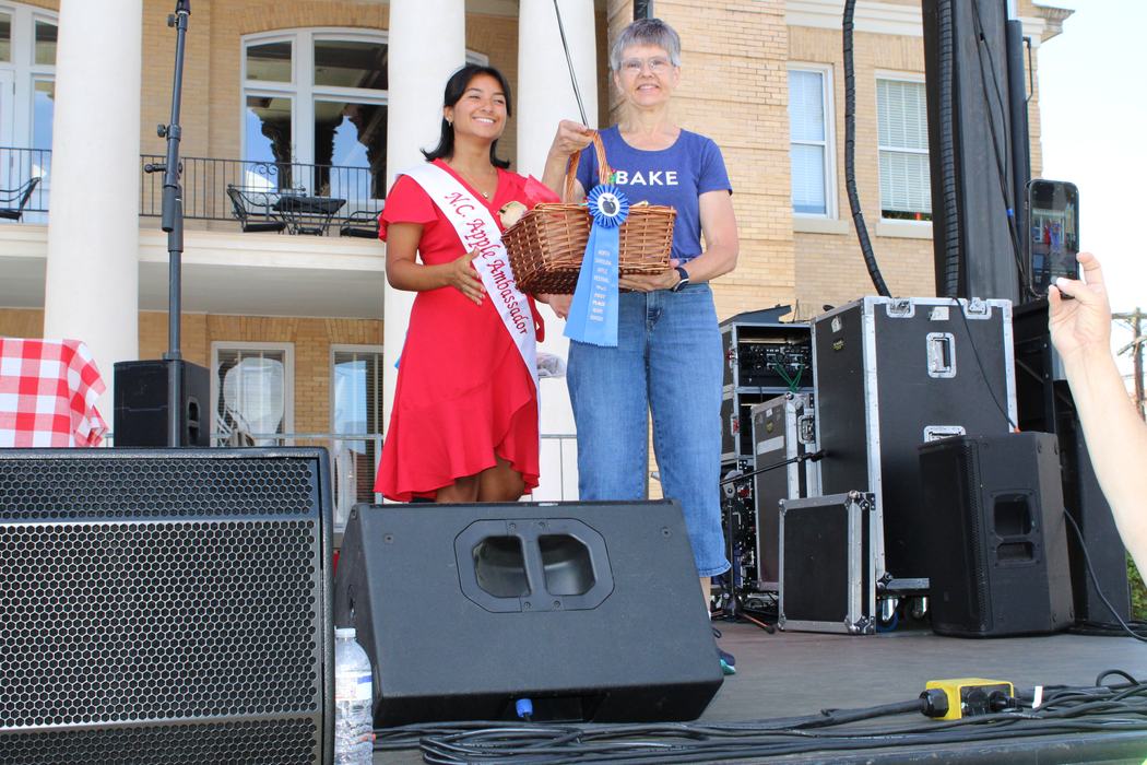 Woman on the left handing gift basket to woman on the right. 