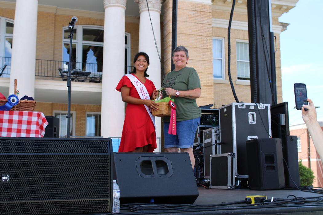 Woman on the left handing gift basket to woman on the right. 