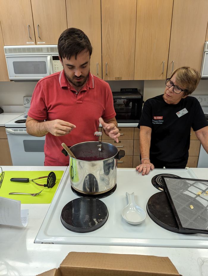 Two people talking in demonstration kitchen with preserves pot on stove
