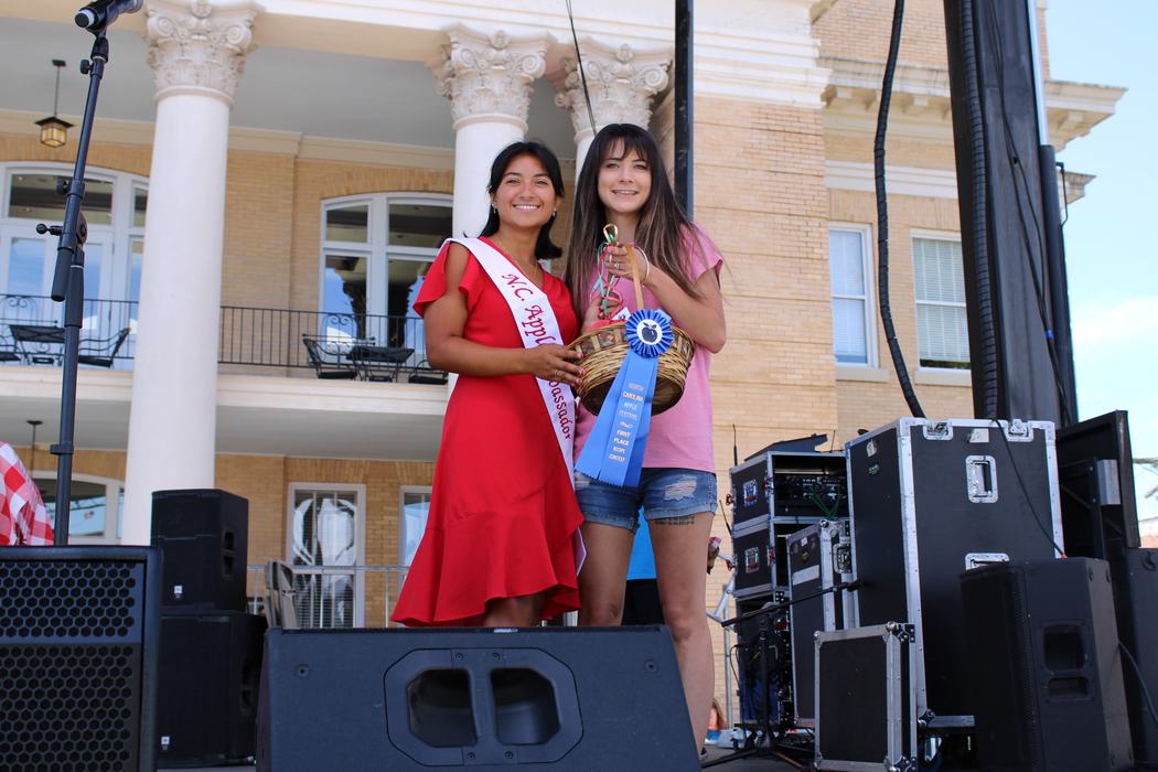 Woman on the left handing gift basket to woman on the right. 