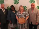 man in suit, woman in dress, woman in dress holding wooden plaque, man in tan jacket