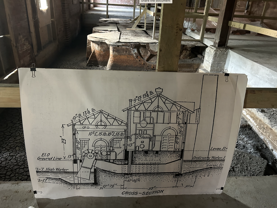 Blueprint labeled "CROSS-SECTION" clipped to a railing, showing a building cross-section in an industrial space.