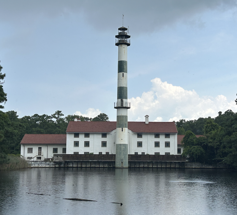Tall green-and-white striped lighthouse rising from center of white building by a lake