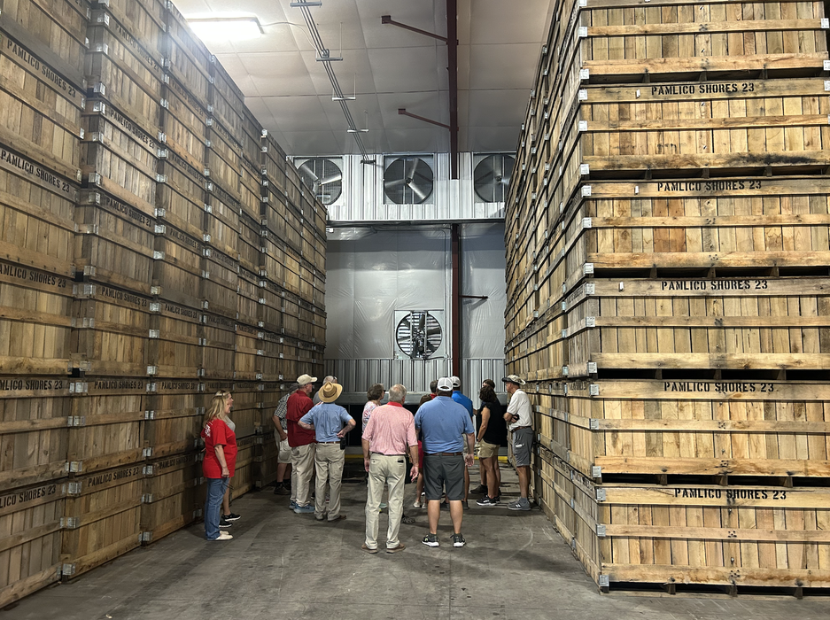 People between tall wooden crates stamped "PAMLICO SHORES 23" in a warehouse