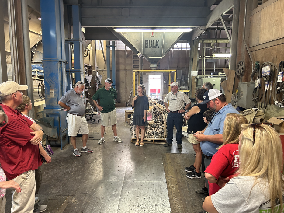 Group standing in industrial warehouse under a large hopper labeled BULK